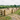A sandschool riding arena with horses and riders. Surrounded by a post and rail fence with a 5-bar entrance gate